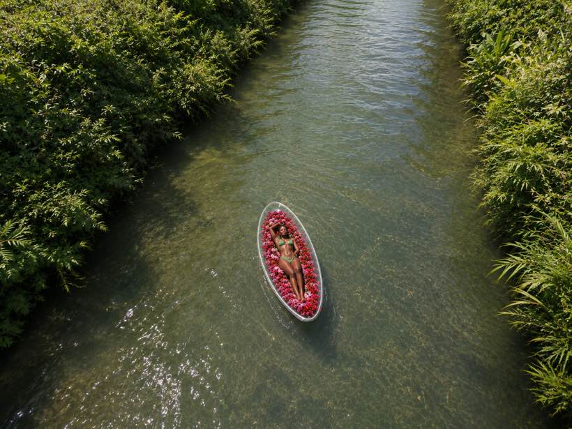 Overhead drone shot of a flower-filled clear kayak on the river