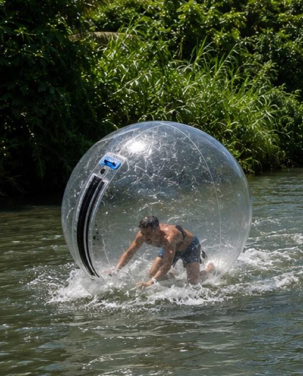 A guest on all fours inside a water walking ball, spray flying